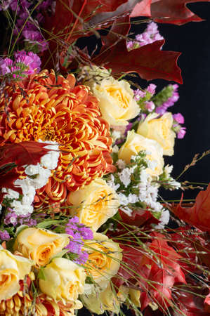 Fragment of a bright autumn bouquet in yellow-orange tones with roses and chrysanthemums with bright leaves on a black background.の写真素材