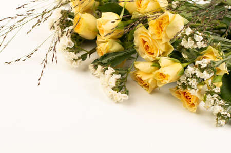 Part of a bouquet of yellow roses and white small flowers and herbs on a white background with space for writing text.の写真素材