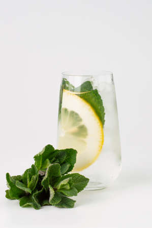 On a light background, a bunch of mint, in the background a blurred image of a chilled drink with ice and a slice of lemon, mint leaves.の写真素材