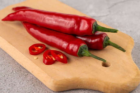 Blurred image of red chili peppers and slices on a wooden board on a gray background.