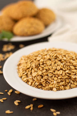 In the foreground, a blurred image of oatmeal in a white plate, in the background oatmeal cookies on...