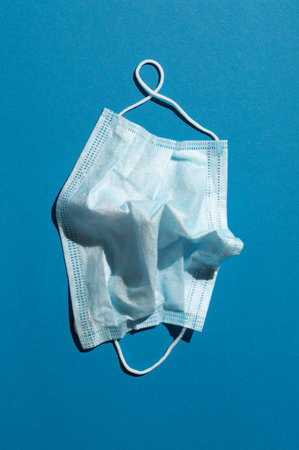 On a blue background, a crumpled medical mask under harsh lighting. View from above.の写真素材