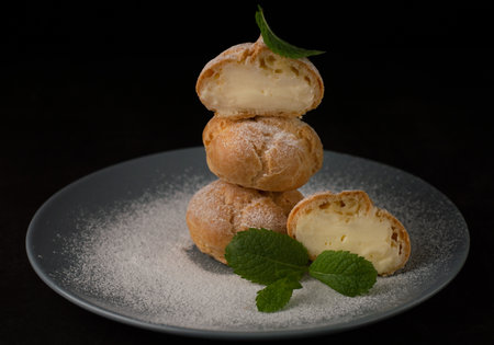 Blurred image of eclairs on a dark background, sprinkled with powdered sugar with mint leaves on a...
