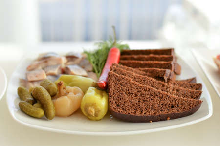 Blurred image of a plate with pickled vegetables, black bread and herring. Catering concept.