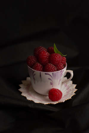 Blurred image of a cup and saucer with raspberries on a black background.の写真素材