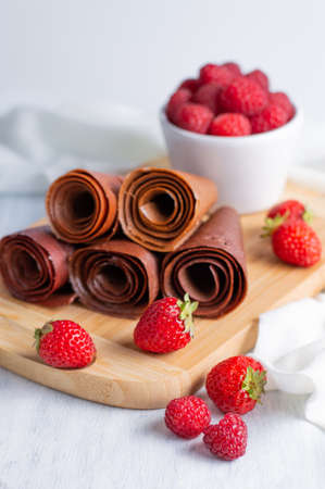 On a light background, a blurred image of rolls of pastille on a plank, strawberries and raspberries in a white plate.の写真素材
