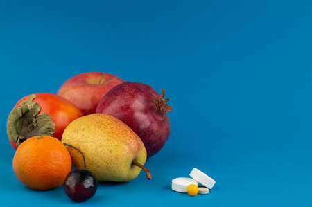 A pile of fruits and pills on a blue background with space for writing text. Medical concept.の写真素材