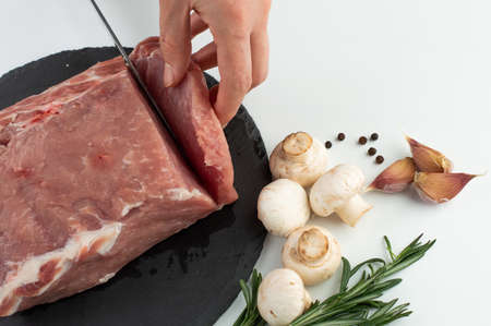 Raw pork tenderloin is sliced ââon a board for cooking.Pork, mushrooms, rosemary, garlic, pepper.の写真素材