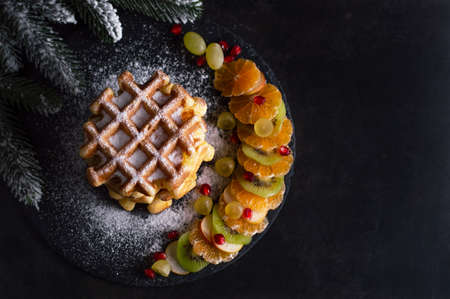 Belgian waffles with powdered sugar and fruits on a dark background with space for writing text. Concept background for Christmas menu or recipe.の写真素材