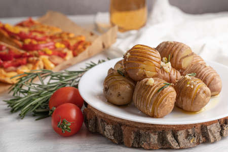 In the foreground is a baked potato on a white plate, tomatoes and rosemary, in the background is a...