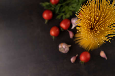 Blurred image of spaghetti, tomatoes, garlic, greens on a black background with space for text.View from above.の写真素材