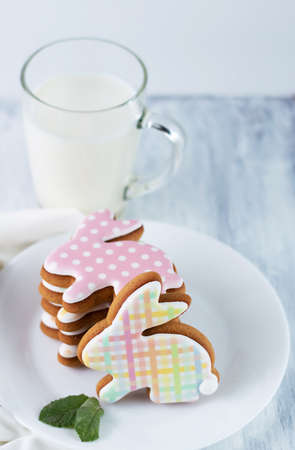 Multi-colored cookies in the form of hares on a plate, a cup of milk on a light background.Calorie...