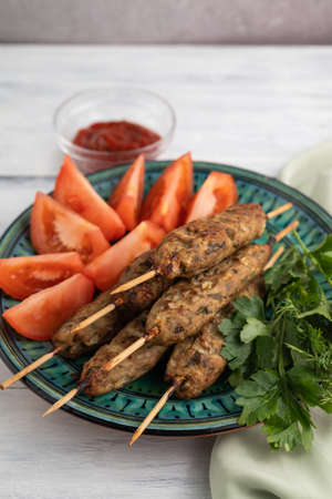 Blurred image of lula kebabs in a plate with tomato slices and greens on a light background. Eastern food.の写真素材