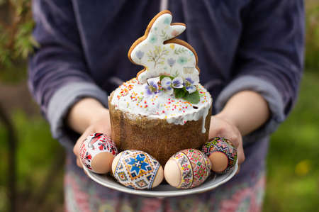 Blurred image of an Easter cupcake, colorful eggs in a plate held by a woman on a background of spring greenery. holiday postcard.の写真素材