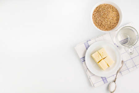 On a light background with a place for writing a text, raw brown rice, a glass of water, a piece of...