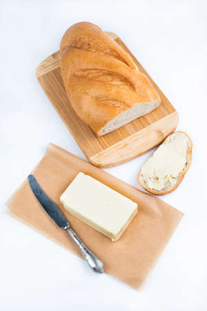 On the white table is butter, a knife on the board is a white loaf and a piece of loaf with...