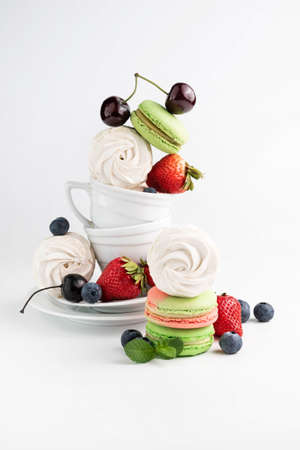 Macaroons and marshmallows in white cups and plates, berries on a light background. still life.の写真素材