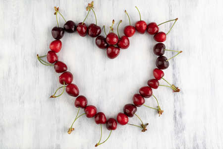 The heart is lined with cherries on a gray wooden background. fruit background.