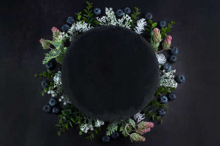 On a dark background, branches with leaves and blueberries are arranged in a circle. Summer background with place for writing text.の写真素材