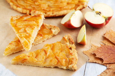 Slices of apple pie, apples, autumn leaves on a light table. The concept of seasonal baking.の写真素材