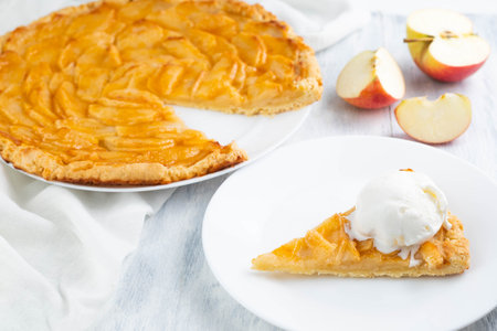 Apple pie and a scoop of ice cream on a plate and apples on a light table. The concept of home baking.の写真素材