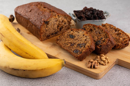 Banana bread on a wooden board, bananas, nuts and raisins on a gray table.The concept of homemade...