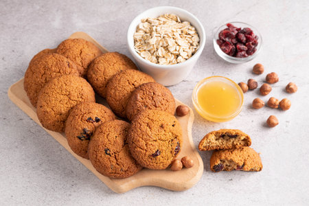 On a gray table are oatmeal cookies, honey, hazelnuts, oatmeal and cranberries in a plate. The concept of cooking healthy pastries.の写真素材