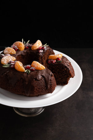 Blurred image of a chocolate cupcake decorated with tangerine slices, pomegranate berries, rosemary sprigs on a dark background. Holiday baking concept.の写真素材