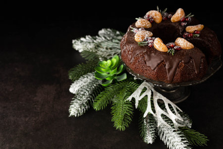 On a dark background with space for text, a chocolate muffin is decorated with tangerines and sprigs of rosemary and sprigs of spruce.の写真素材