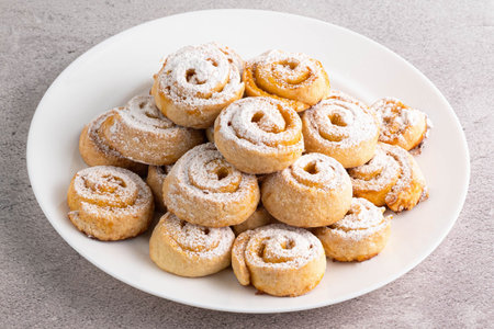 Homemade cookies with filling sprinkled with powdered sugar, in a gray plate on the table. home...