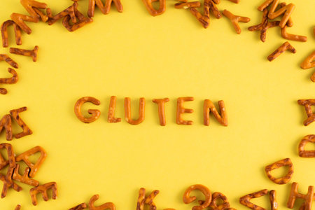 On a yellow background, the word gluten is folded from cookies. The concept of carbohydrates.の写真素材