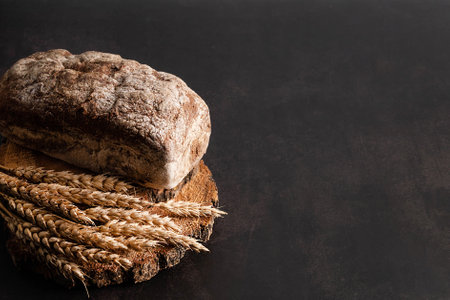On a dark background with space for writing text, a blurred image of ears of corn and dark bread. Background for writing a recipe.の写真素材