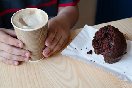 On the table is a piece of muffin in a paper plate and a latte in the hands of a guy in a fast food cafe.Carbohydrate fast food concept.の写真素材