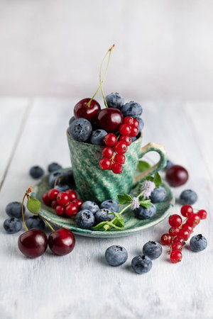 Blueberries, red currants, cherries in a green ceramic cup on a light background. Summer still life.の写真素材