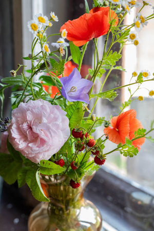 A delicate bouquet with a rose and wildflowers and berries on the windowsill in an old house.の写真素材