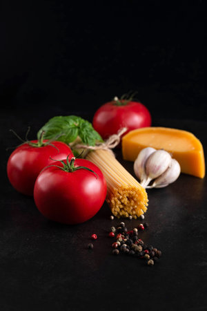 On a dark background, ingredients for cooking spaghetti with tomato sauce and parmesan.の写真素材