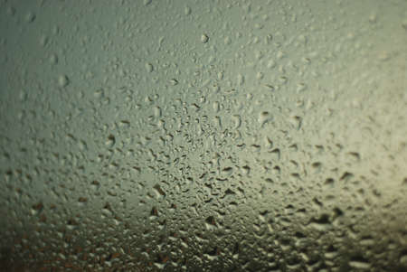 Drops of water flow down the surface of transparent glass.の写真素材