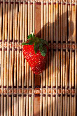 one large red strawberry on a bamboo lunch mat close-upの写真素材