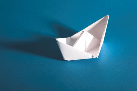 wtite paper yacht with shaodow on blue background