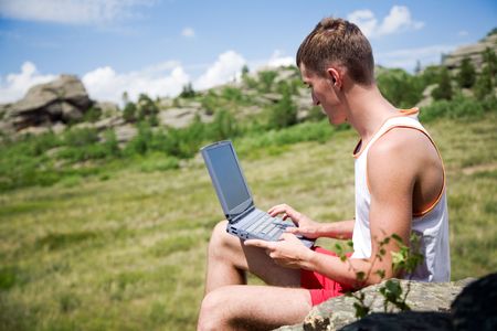 Young man with laptop against summer landscapeの写真素材