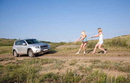two young beauty girl tugging car on the solitary roadの写真素材