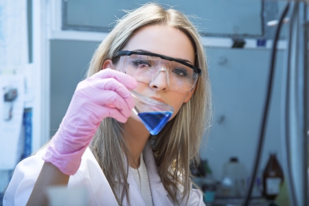 female researcher look at retort with blue liquidの写真素材