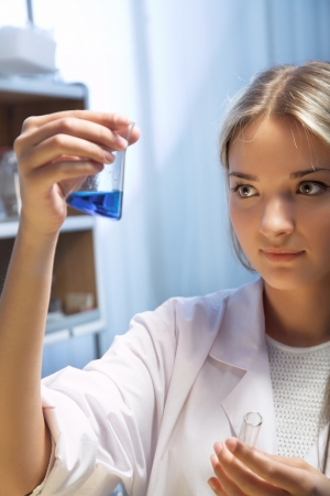 female researcher look at retort with blue liquidの写真素材