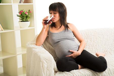Young pregnant woman drinks a juice on the sofaの写真素材