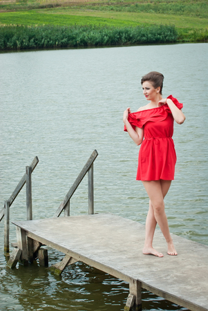 Girl on the pier at the lake in summer in red dressの写真素材