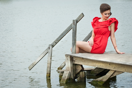 Girl on the pier at the lake in summer in red dressの写真素材