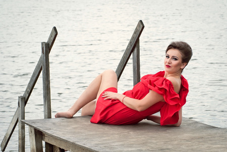 Girl on the pier at the lake in summer in red dressの写真素材