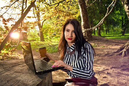 The girl sits with a laptop in the nature in the summer or in the fallの写真素材