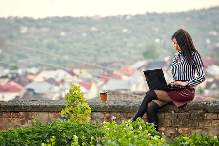 The girl sits with a laptop in the nature in the summer or in the fallの写真素材