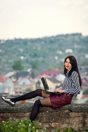 The girl sits with a laptop in the nature in the summer or in the fallの写真素材